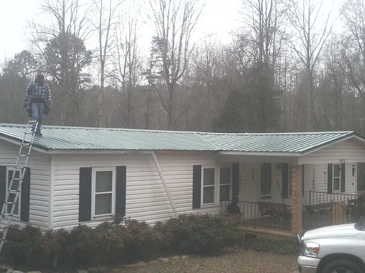 Worker on a ladder beside a new green metal roof on a ranch home in Burkittsville