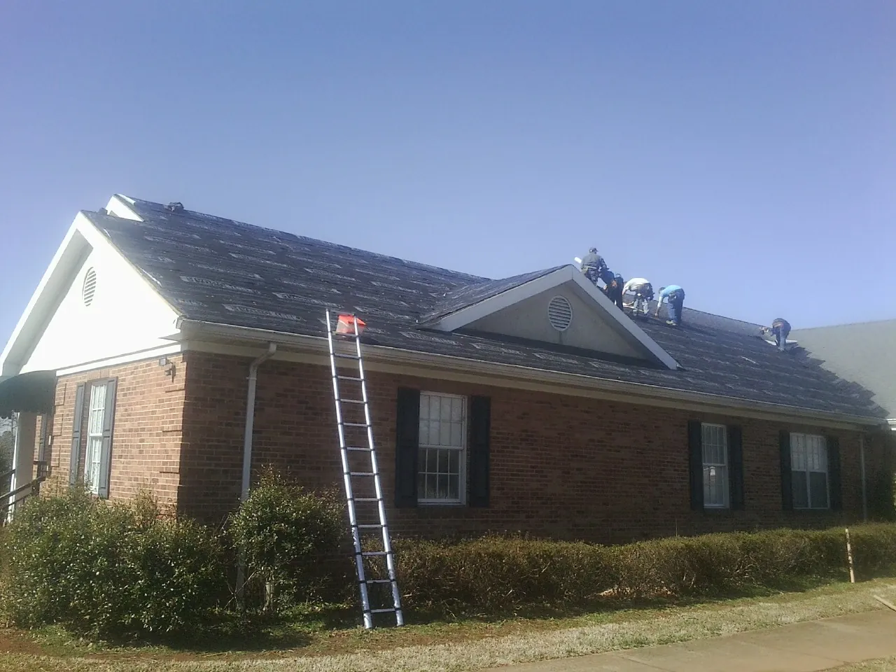 Crew tearing shingles off a brick ranch roof with a ladder set — Metal Roof Repair work by our crew in Burkittsville