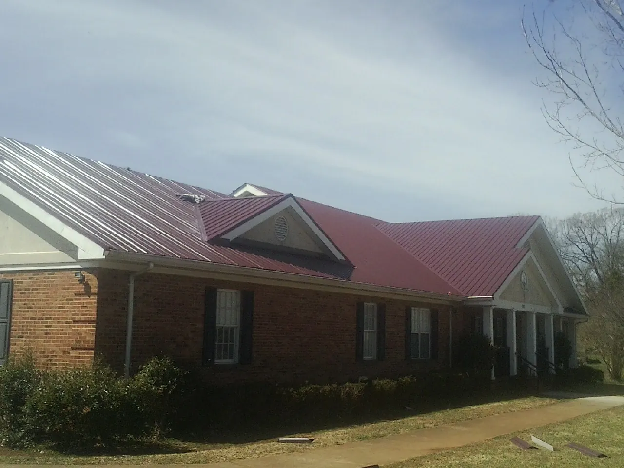 Red metal roof with gabled entries on a long brick building, from a Hail Damage Roof Repair job in Burkittsville