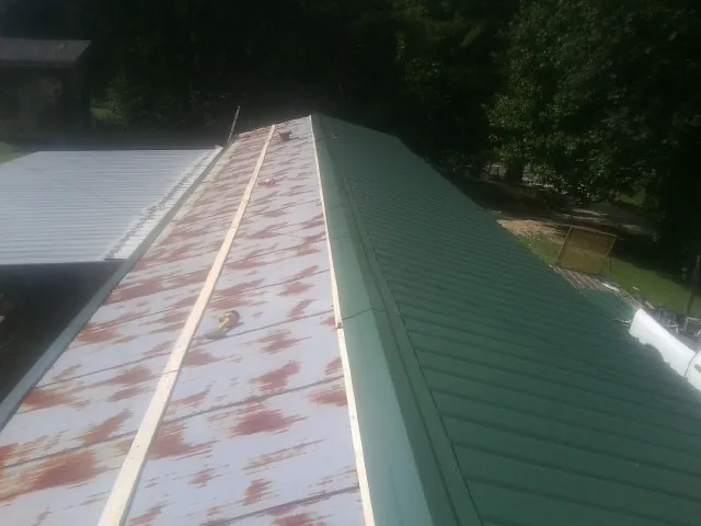 Old rusted panels beside newly installed green metal roofing — Wind Damage Roof Repair by Roofing Brothers in Burkittsville