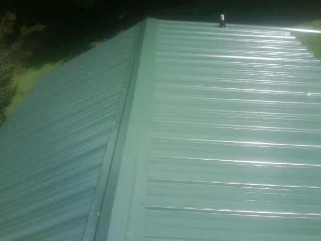 New green metal panels meeting at the ridge of a roof — Flat Roof Repair work by our crew in Burkittsville