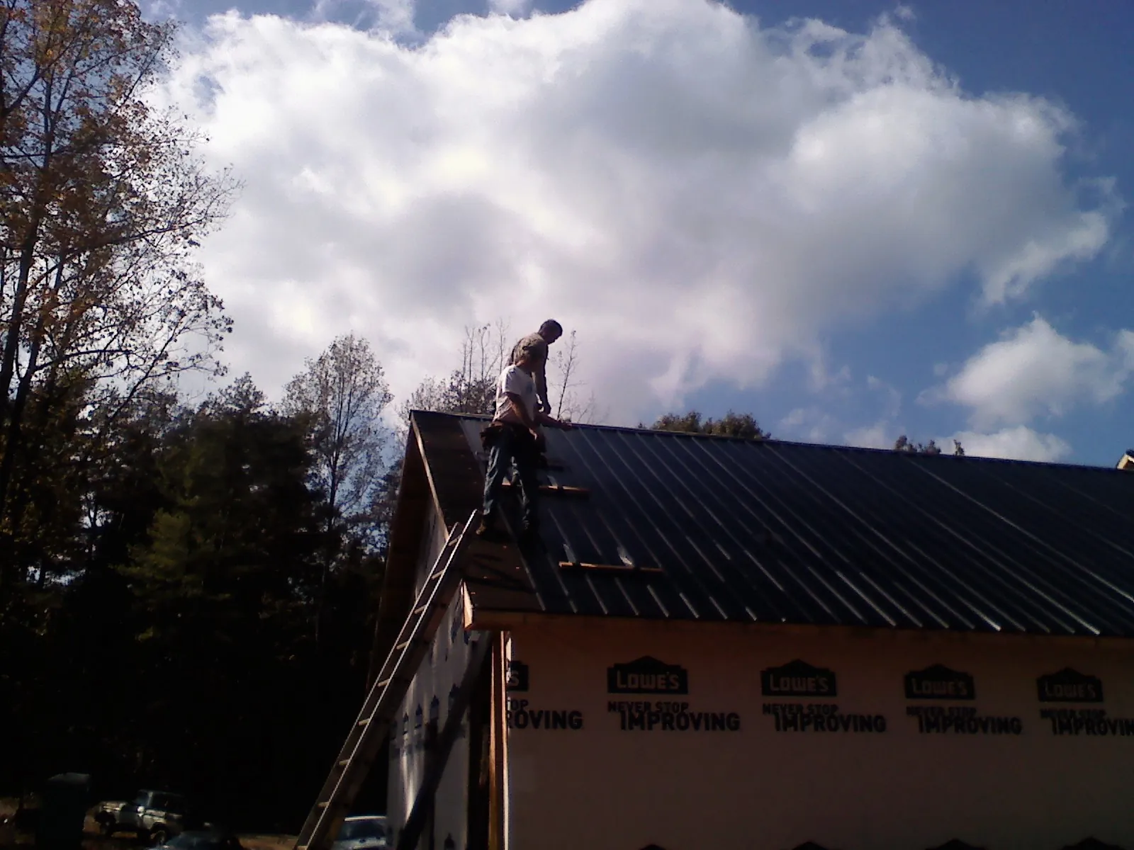 Roofer fastening dark metal panels high against a cloudy sky, from a Roof Inspection job in Burkittsville