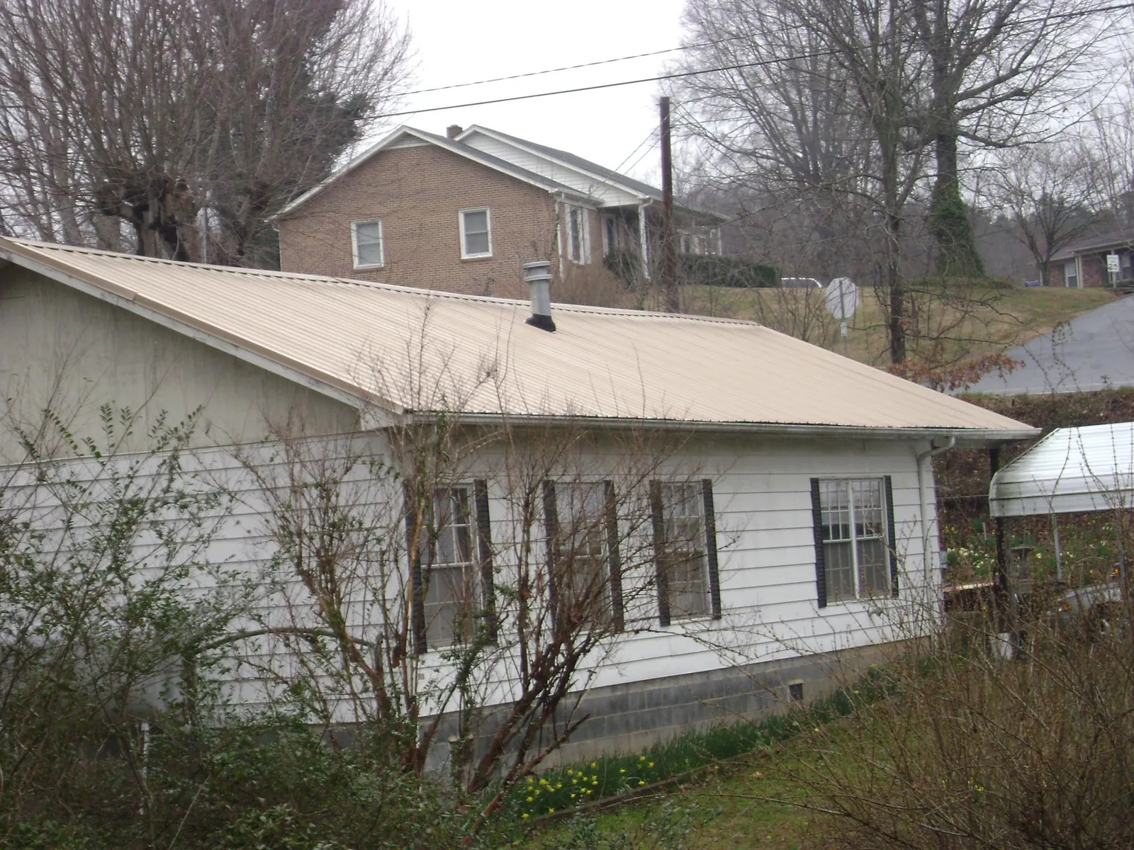 Tan metal roof on a white sided house set into a hillside — Commercial Roofing by Roofing Brothers in Burkittsville